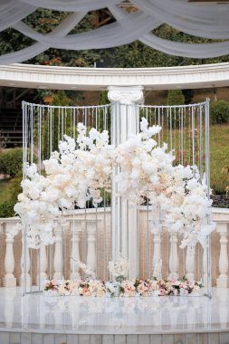 Çiçekleri ve gümüş sütunu olan beyaz bir kemer yolu. Kemer yolu görüntünün tam ortasında ve sütun da sağ tarafta.