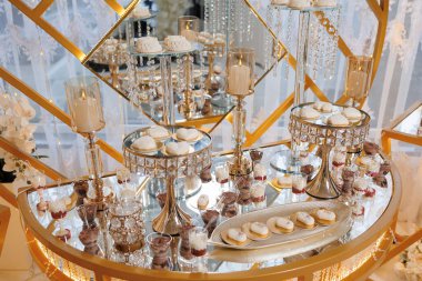 Kekler ve kurabiyeler de dahil olmak üzere çeşitli tatlı ve hamur işleri içeren bir masa altın çerçeveli bir odaya kuruluyor. Tatlılar gümüş tepside dizilir ve mumlarla çevrilidir.