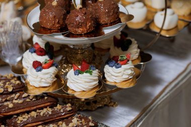 Pasta, pasta ve meyve gibi çeşitli tatlıların olduğu bir masa. Tatlılar altın kaplama bir stantta düzenlenir ve çikolatanın da dahil olduğu bir çok farklı pasta çeşidi vardır.