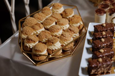 Bir tepsi hamur işi bir tabak browninin yanında bir masada oturur. Pastalar küçük ve altın renkli, browniler de çikolatalı ve şekerli. Masa özel bir durum için hazırlandı.