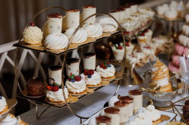 Pasta, kek ve hamur işleri dahil bir masa dolusu tatlı. Tatlılar beyaz bir masa örtüsü üzerinde dairesel bir düzende dizilmiştir.