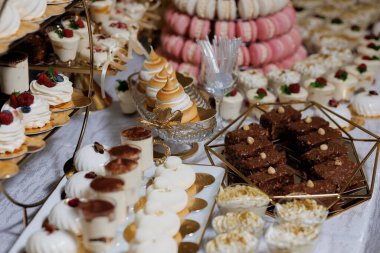 Pastalar, kurabiyeler ve brownilerle dolu bir masa. Tatlılar onları lezzetli ve davetkar gösterecek şekilde düzenlenmiş.