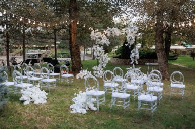 Bir parkta büyük bir açık hava düğün töreni düzenleniyor. Sandalyeler sıraya dizildi ve konuklar yerleşti. Sandalyeler bembeyaz ve ayarı da ışıklarla aydınlatılıyor.