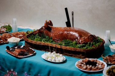 Üzerinde büyük bir rosto ve çeşitli yiyecekler olan bir masa. Sahne şenlikli ve kutlayıcıdır.