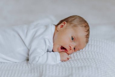 Bir bebek ağzı açık bir şekilde yatakta yatıyor. Bebek gülümsüyor ve mutlu.