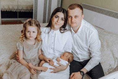 Dört kişilik bir aile, bir bebek de dahil, bir yatakta oturuyor. Bebek bir kadın tarafından tutuluyor. Sahne sıcak ve sevgi dolu, çünkü aile, ailelerine yeni katılan kişiyi kutlamak için bir araya geldi.