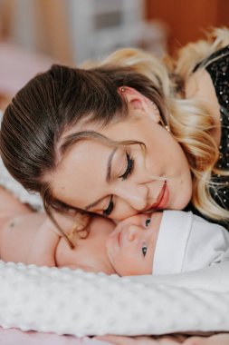 Bir kadın göğsünde bir bebekle uzanıyor. Bebek beyaz bir şapka takıyor.