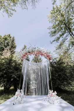 Pembe çiçekli ve beyaz şeritli beyaz bir kemer. Kemer yolu arka planda ağaçlar olan bir parkta.