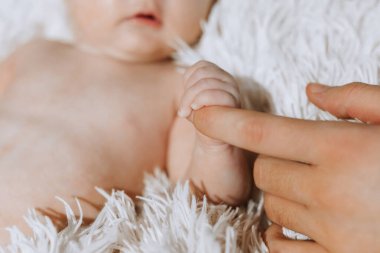 Bir bebeğin eli bir bebeğin yüzüne doğrultulur. Bebek beyaz bir battaniyenin üzerinde yatıyor.