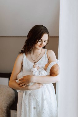 Bir kadın kucağında bir bebek tutuyor. Bebek beyaz bir battaniye giyiyor.