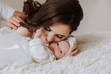 Bir kadın kucağında bir bebek tutuyor. Bebek beyaz bir şapka giyiyor. Kadın yüzünde bir gülümsemeyle bebeğe bakıyor.