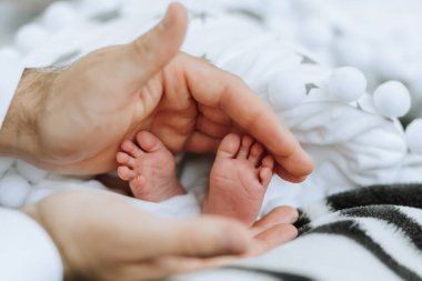 Bir bebeğin ayakları bir erkeğin ellerinde tutuluyor. Bebek küçük ve kırılgan, ve adam koruma ve rahatlık sağlıyor. Sıcaklık ve bakım kavramı
