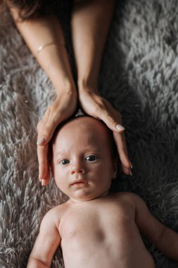 Bir bebek battaniyeye uzanmış, kafası iki kişinin ellerinin arasındadır. Bebek tuhaf bir ifadeyle kameraya bakıyor. Bebek arasındaki sıcaklık ve şefkat kavramı.
