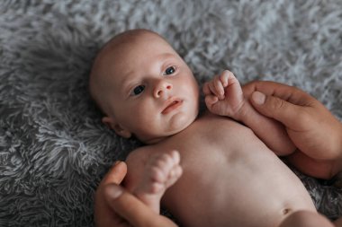 Bir bebek başı yana eğilmiş bir battaniyenin üzerinde yatıyor. Bebeğin gözleri açık ve o da kameraya bakıyor. Bebeğin yüzü gülümsüyor ve elleri göğsüne konuyor.