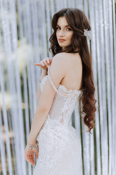 A woman in a white dress with long hair is posing for a photo. The photo is in black and white and has a vintage feel to it. The woman's pose and the dress give off a sense of elegance