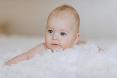 Bir bebek başı yana eğilmiş beyaz bir battaniyenin üzerinde yatıyor. Bebeğin gözleri kapalı ve dinleniyor.