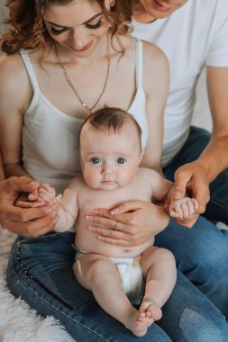 Bir bebek anne ve babasıyla birlikte bir yatakta oturuyor. Bebek, babasının elini tutuyor.