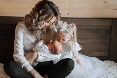 İki küçük kız kucağında otururken bir kadın kucağında bebek tutuyor. Sahne sıcak ve sevgi dolu, çünkü aile, ailelerine yeni katılan kişiye bağlanıyor.