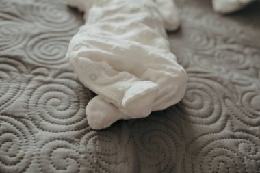 Beyaz elbiseli bir bebek yatakta yatıyor. Bebeğin ayakları görünür durumda ve bebeğin bacakları kıvrılmış. Bebek yumuşak ve rahat kıyafetler giydiği için masumiyet ve sıcaklık kavramı.