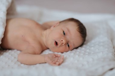 Bir bebek gözleri tamamen açık beyaz bir battaniyenin üzerinde yatıyor. Bebeğin yüzü görüntünün ana odak noktasıdır ve bir şaşkınlık ya da merak durumundadır. Masumiyet ve merak kavramı