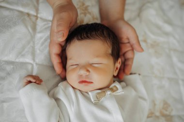 Bir bebek, kafası bir insanın göğsünde dinlenen bir yatakta uyur. Bebek beyaz bir gömlek ve bir papyon giyiyor. Bebek kucağındayken sıcaklık ve konfor kavramı.