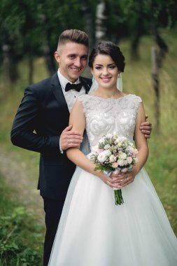 Bir gelin ve damat tarlada fotoğraf çektirmek için poz veriyorlar. Gelin elinde bir buket çiçek tutuyor.