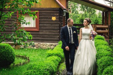 Bir gelin ve damat evin önünde bir patikada yürüyorlar. Gelin beyaz bir elbise giyiyor ve damat bir takım elbise giyiyor. El ele tutuşuyorlar ve mutlu görünüyorlar.