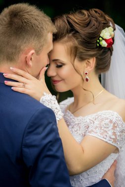 Gelin ve damat birbirlerini kucaklıyor, gelin beyaz bir elbise ve damat mavi bir takım elbise giyiyor.