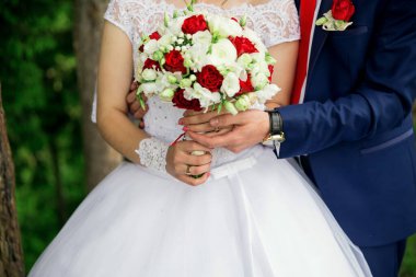 Bir gelin ve damat el ele tutuşuyor ve bir buket kırmızı ve beyaz çiçek. Gelin beyaz bir elbise giyiyor ve damat mavi bir takım elbise giyiyor. Aşk ve mutluluk kavramı