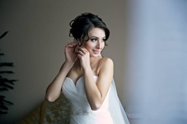 Beyaz gelinlikli bir kadın düğünü için hazırlanıyor. Aynada kendine bakıyor ve saçını düzeltiyor.