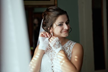 Bir kadın düğün için hazırlanıyor ve gelinliğini giyiyor. Beyaz bir elbise ve duvak takıyor.