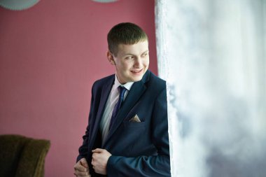 Takım elbiseli bir adam kameraya gülümsüyor. O mavi bir takım elbise ve mor bir kravat takıyor.