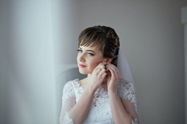 Bir kadın kulaklarını deldiriyor. Beyaz bir elbise ve duvak takıyor. Görüntüde hafif ve havadar bir hava var.