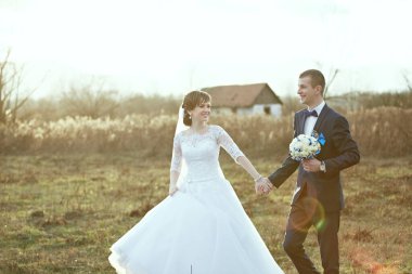 Bir gelin ve damat bir tarlada birlikte yürüyorlar. Gelin beyaz bir elbise giyiyor ve damat mavi bir takım elbise giyiyor. El ele tutuşup kameraya gülümsüyorlar.