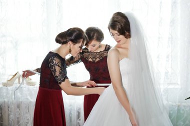 Üç kadın düğün için hazırlanıyor. Kadınlardan biri gelinin elbisesini ayarlıyor.