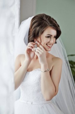 Bir gelin düğünü için hazırlanıyor ve gelinliğini giyiyor. Gülümsüyor ve kameraya bakıyor.