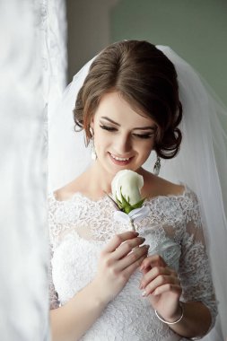 Bir gelin elinde beyaz bir gül tutuyor. Gülümsüyor ve kameraya bakıyor.