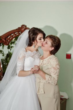 Bir gelin annesinin elini öper. Anne beyaz bir elbise giyiyor.