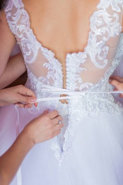 Bir kadın gelinliğin dantelini ayarlıyor. Elbise beyaz ve dantel tasarımı var.