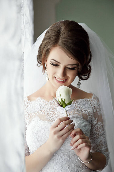 Невеста держит в руке белую розу. Она улыбается и смотрит в камеру.