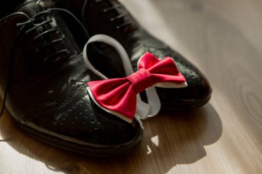 Üzerinde kırmızı papyon olan bir çift siyah ayakkabı. Papyon ayakkabıya bir kalbe benzeyecek şekilde bağlanmış. Ayakkabılar ve papyon ahşap bir zemine konur.