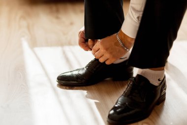 Bir adam ayakkabılarını ve çoraplarını giyiyor. Bileğinde gümüş bir bilezik var.