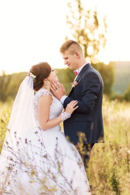 Gelin ve damat, gelin beyaz bir elbise ve damat takım elbise giyerek bir tarlada duruyorlar. Sahne romantik ve mutlu, çünkü çift birbirini kucaklıyor.