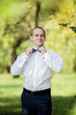 Beyaz gömlekli ve mavi pantolonlu bir adam papyonunu bağlamaya hazırlanıyor. Özel bir durum için formalite ve hazırlık kavramı