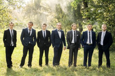 Takım elbiseli bir grup adam tarlada duruyor. Hepsi kravat takıp kameraya bakıyor. Sahne resmi ve profesyoneldir.