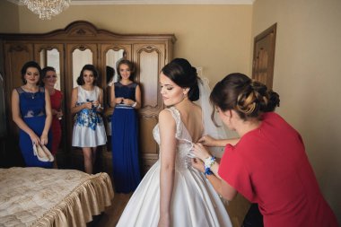 Bir gelin nedimeleriyle düğününe hazırlanıyor. Bir kadın elbisesini ayarlamasına yardım ediyor.