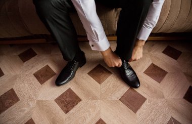 Bir adam ayakkabılarını ahşap bir zeminde giyiyor. Zeminde kare ve daireler var.