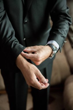 Takım elbiseli bir adam gömleğini düzeltiyor. Bir saat ve bileklik takıyor.