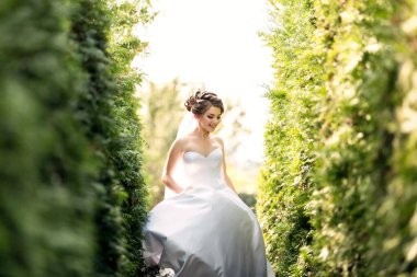 Beyaz elbiseli bir gelin bahçede yürüyor. Gülümsüyor ve gökyüzüne bakıyor.