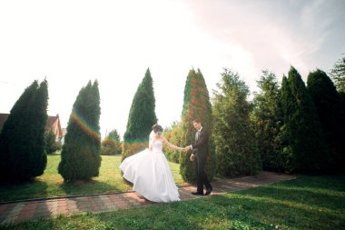 Bir gelin ve damat parkta bir patikada yürüyorlar. Gelin beyaz bir elbise giyiyor ve damat bir takım elbise giyiyor. Sahne mutlu ve romantik.